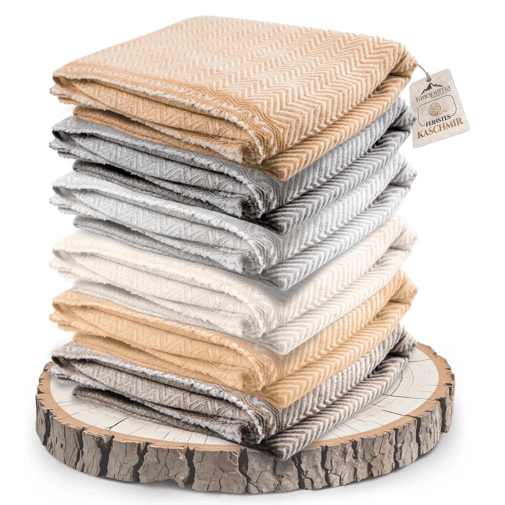 Auf dem Bild sind mehrere gefaltete Decken in verschiedenen Beige-, Grau- und Cremetönen zu sehen. Jede Decke hat ein deutlich erkennbares Fischgrätenmuster. Die Decken sind übereinandergestapelt und liegen auf einer runden Holzscheibe mit sichtbarer Rinde und Jahresringen. An der obersten Decke hängt ein Etikett mit der Aufschrift „Feinstes Kaschmir“. Die Kanten der Decken sind weich und leicht fransig. Das Bild ist hell ausgeleuchtet und wirkt stilvoll arrangiert.
